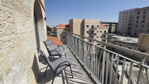 Un balcon avec deux chaises et une petite table, d’où l’on peut admirer un paysage urbain avec ses bâtiments et un ciel dégagé.