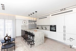 Una cocina moderna con encimera de mármol, taburetes negros, horno integrado e iluminación colgante.