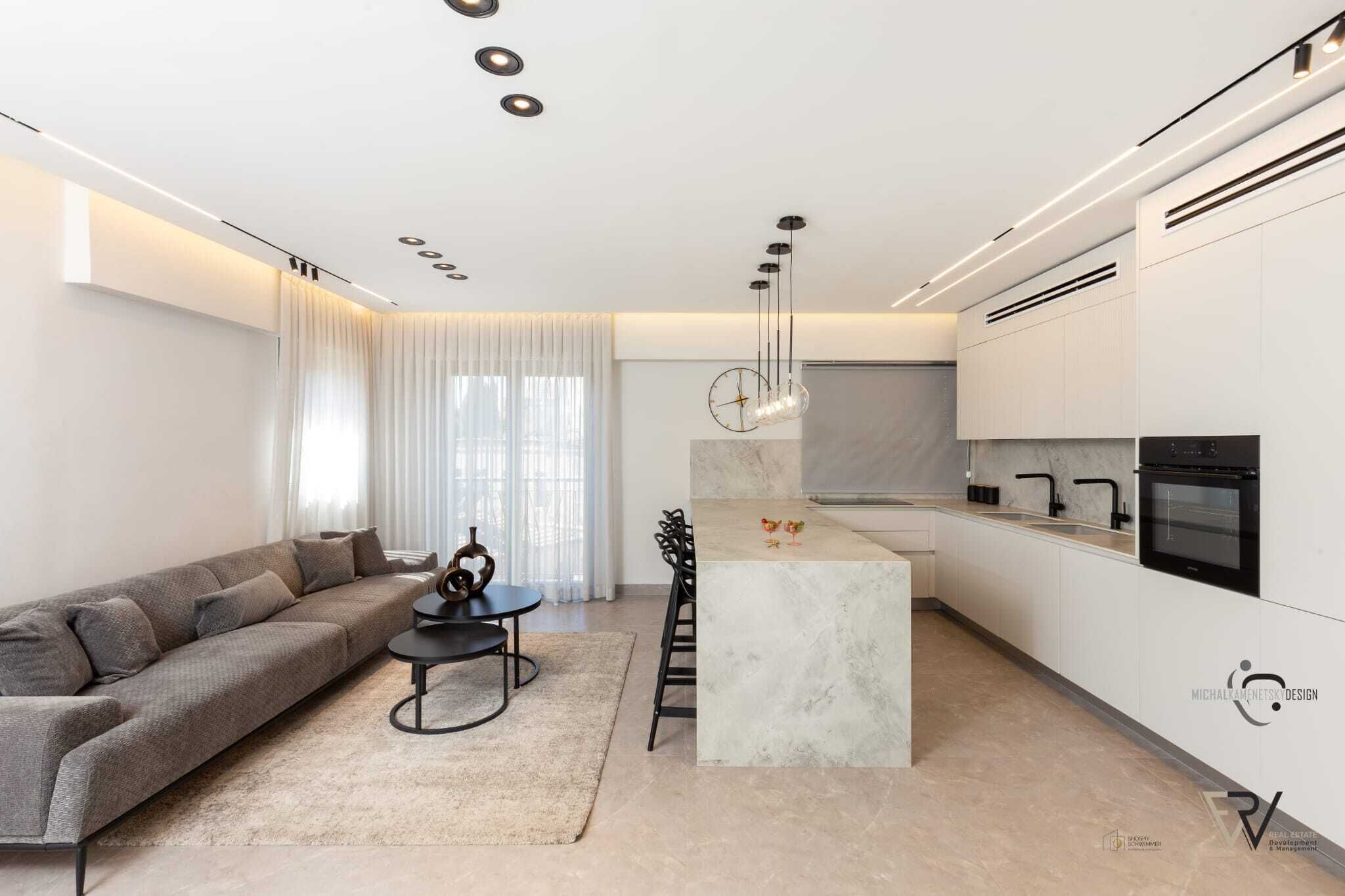 Eine moderne Küche mit einer zentralen Kochinsel, ein Essbereich mit einer Couch und einem Couchtisch sowie ein Wohnzimmer mit einem großen Fenster.
