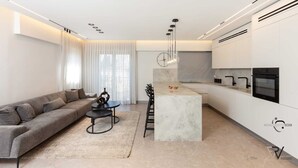 Une cuisine moderne avec des meubles blancs, un îlot en marbre et une cuisinière noire.