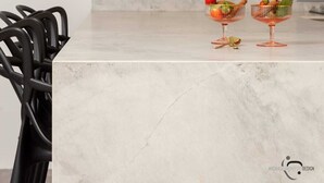 Une cuisine moderne avec un plan de travail en marbre, deux verres à fruits, une chaise noire et une horloge murale.