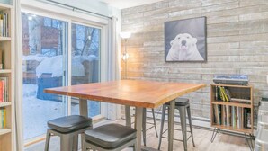 Un comedor con una mesa y taburetes de madera, una estantería y un cuadro en la pared.