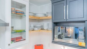 Una cocina moderna con armarios blancos, horno empotrado y un mueble de almacenaje con puerta de cristal.