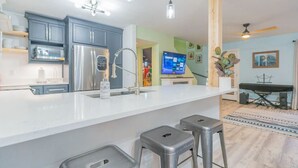 Una cocina moderna con encimera blanca, electrodomésticos de acero inoxidable y taburetes de bar.