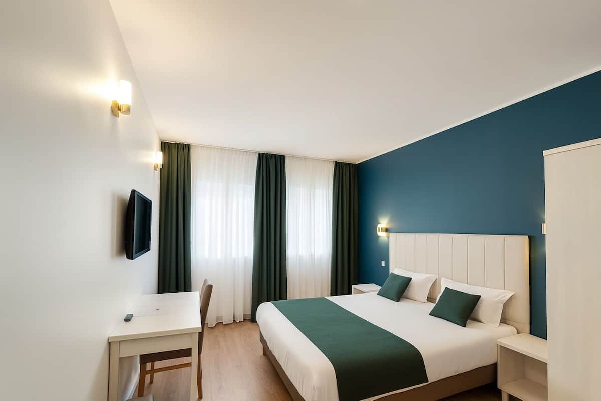 Habitació d'hotel amb llit, escriptori, cadira i televisió.