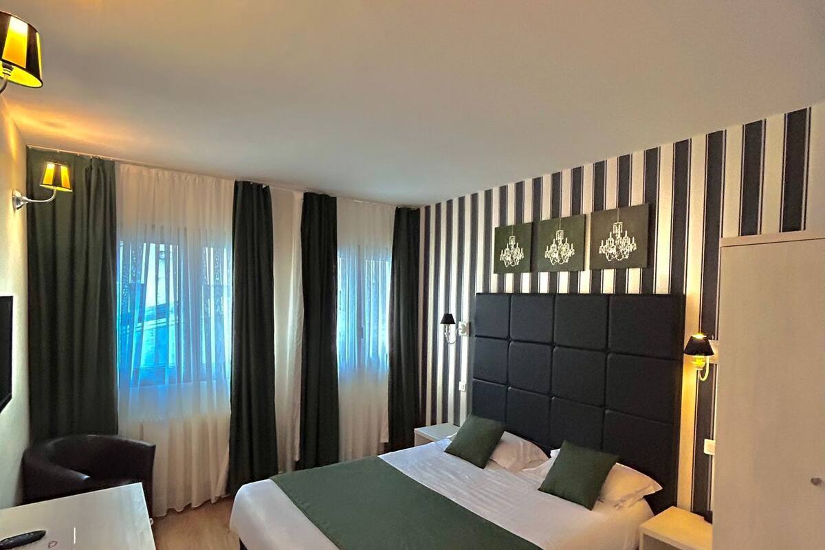 Relax in a stylish room with a large bed, bedside table, and comfortable chair, surrounded by striped wallpaper and wall-mounted lamps.