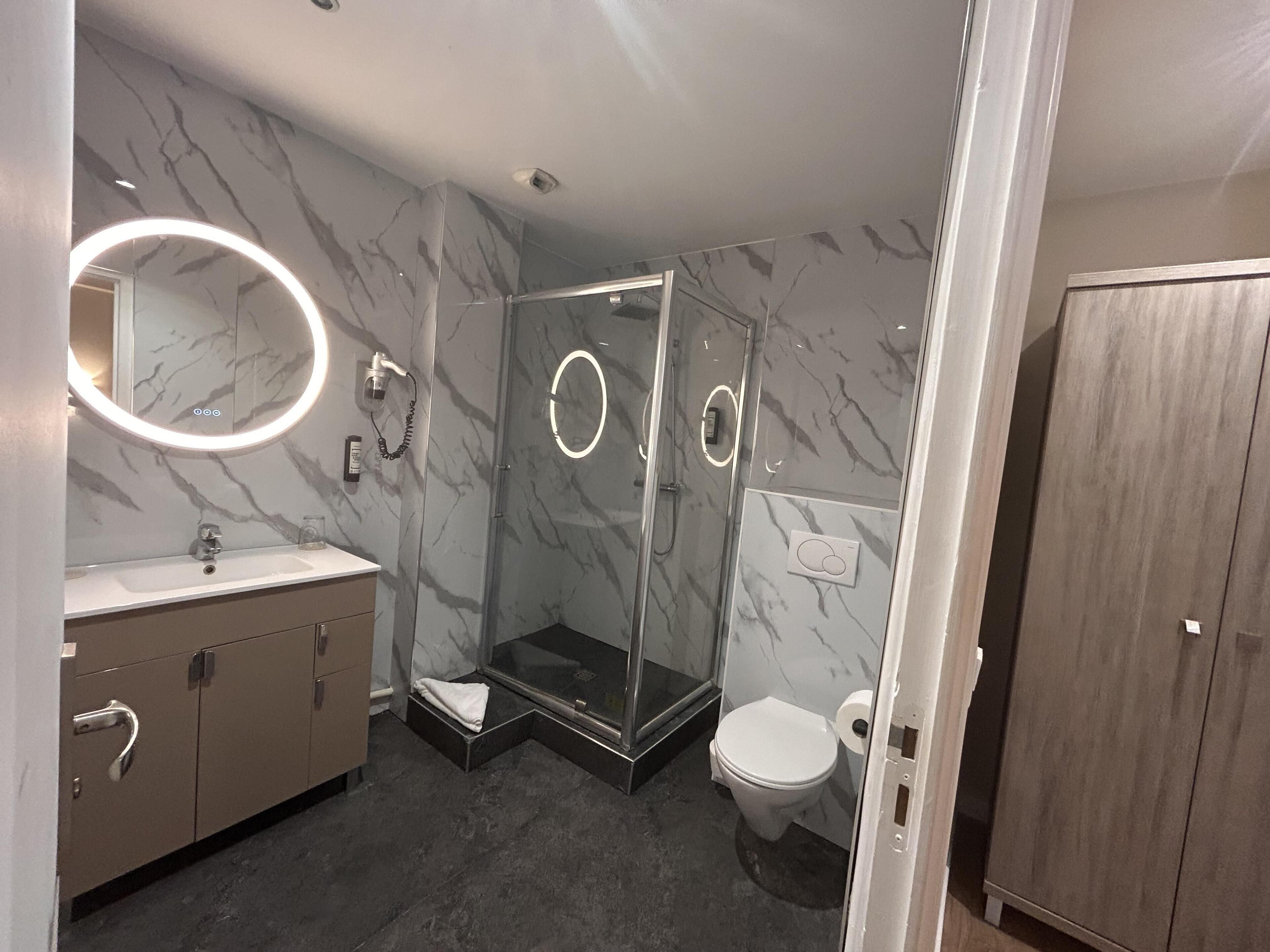 A modern bathroom with a marble wall, a glass shower enclosure, a toilet, and a vanity with a mirror.