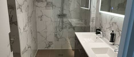A modern bathroom with marble walls, a walk-in shower, and a large mirror.