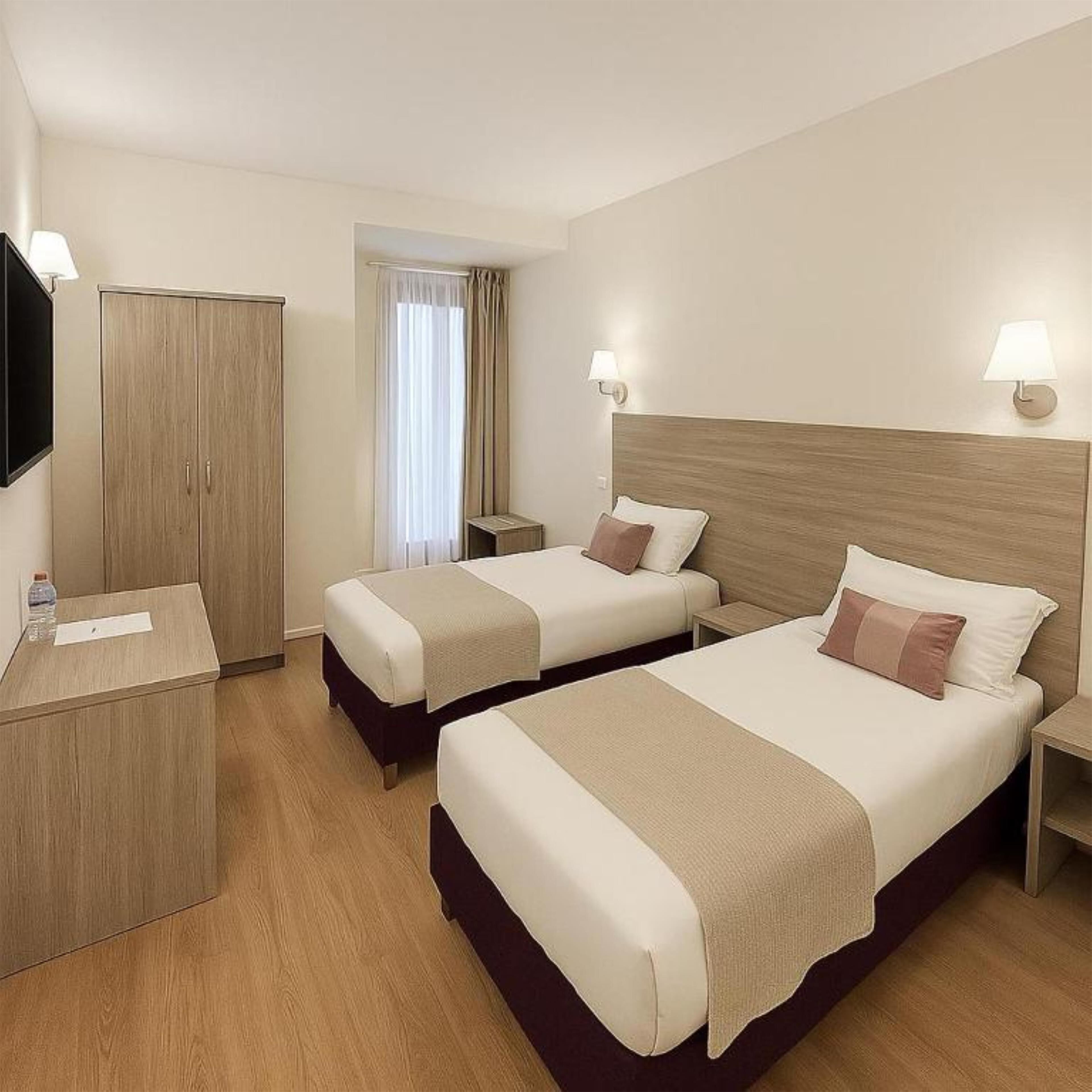 A hotel room with two beds, a wardrobe, a TV, and a window with curtains.