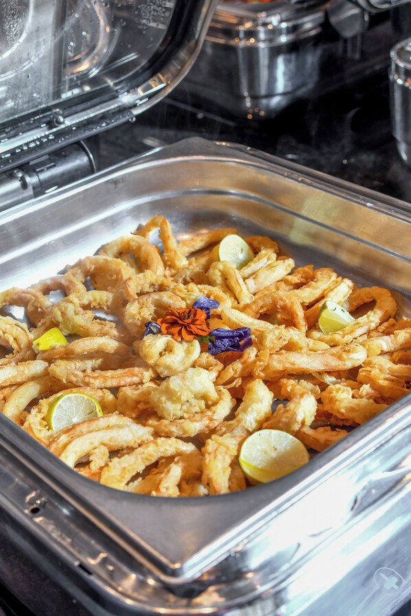 A buffet with fried seafood, garnished with lime and edible flowers.