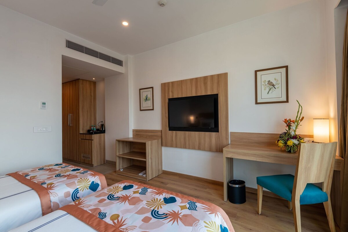 A hotel room with two beds, a desk, a TV, and a small seating area.