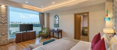 A hotel room with a large bed, a TV, a desk, a chair, and a view of the city.