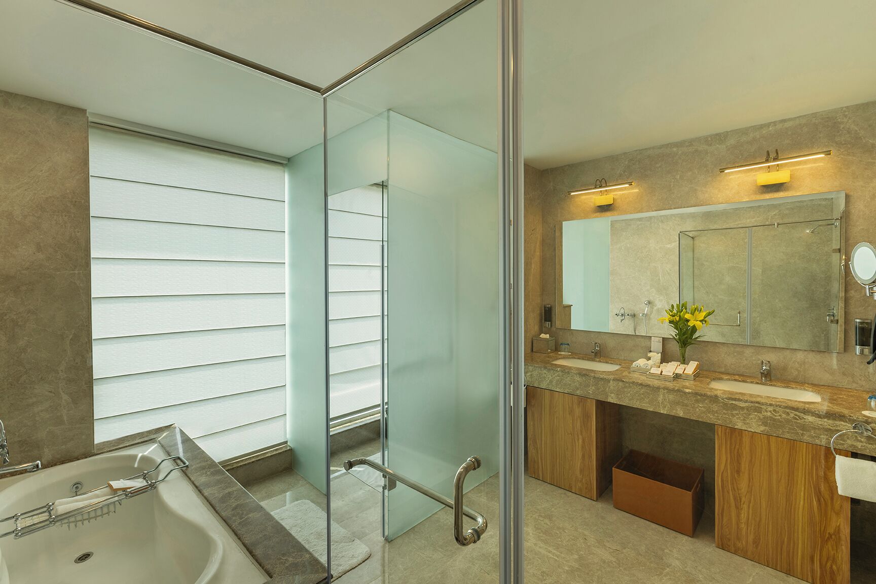 A modern bathroom with a glass partition, a large mirror, and a vanity with a marble countertop.