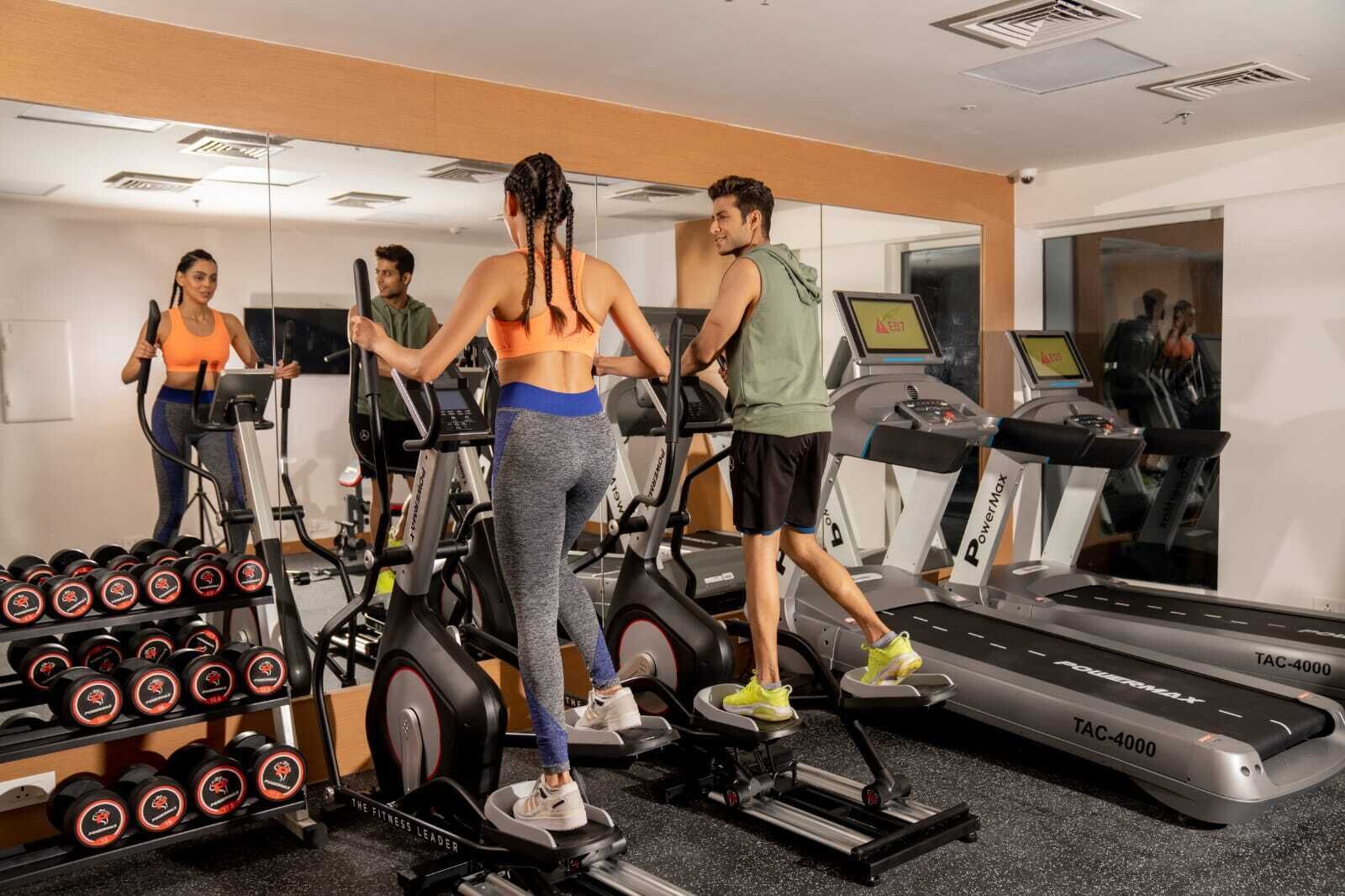 Un gimnasio con cintas de correr, elípticas y una barra de mancuernas.