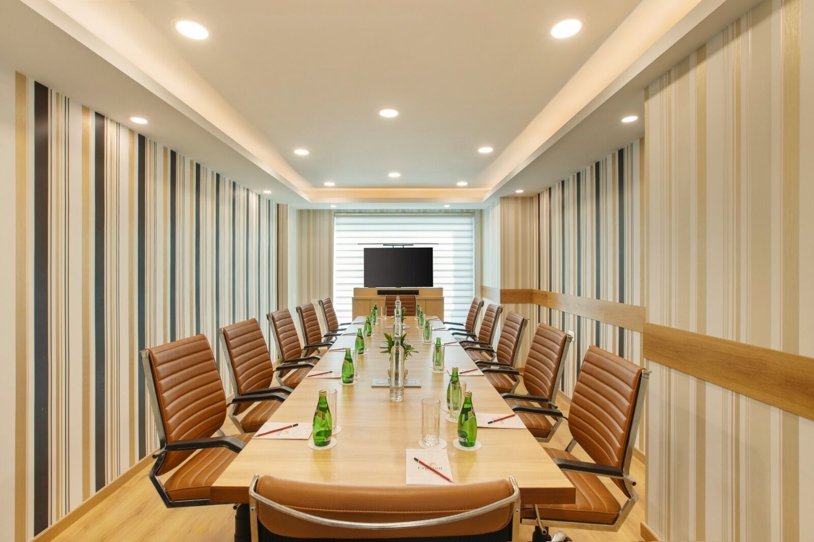 A conference room with a long table, brown leather chairs, and a large screen at the front.