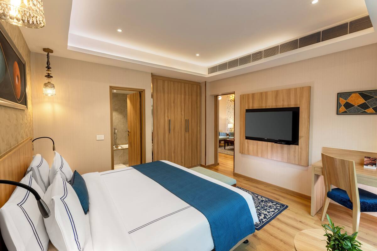 A modern hotel room with a large bed, a desk, a flat-screen TV, and a shower area.