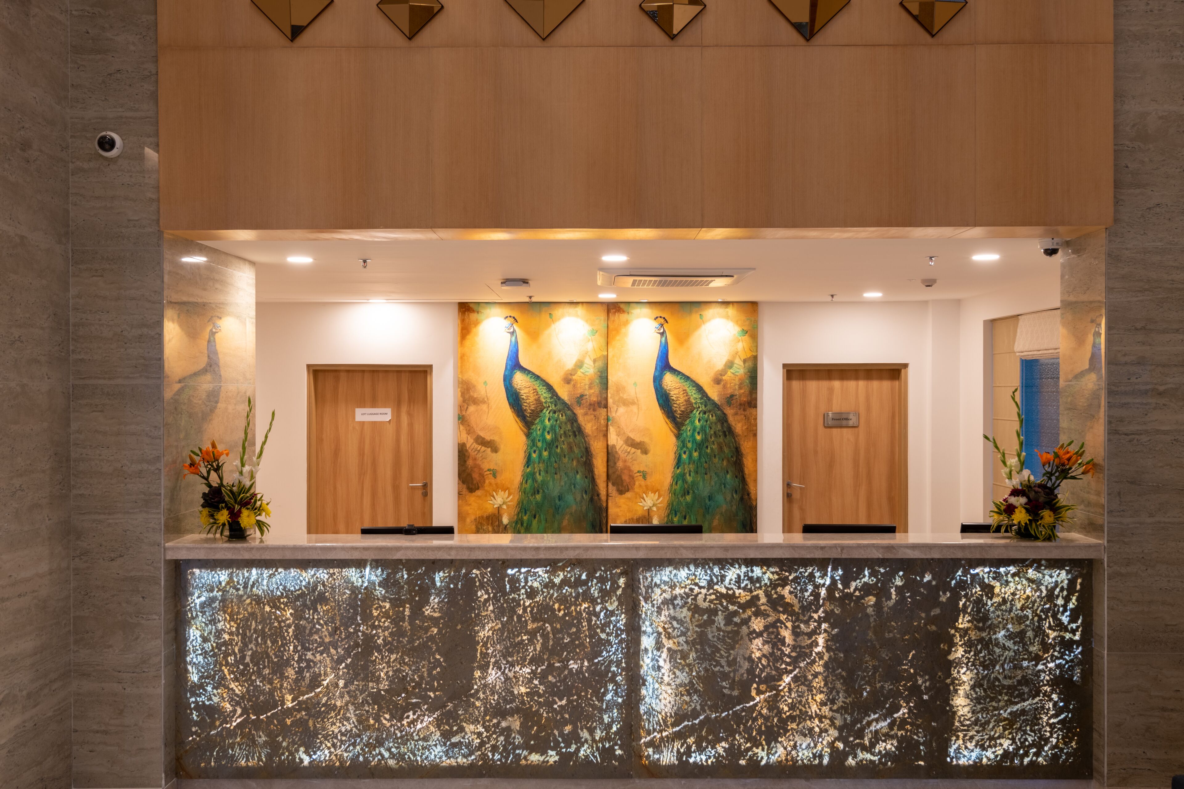 A reception area with a large peacock painting, wooden doors, and a reception desk.