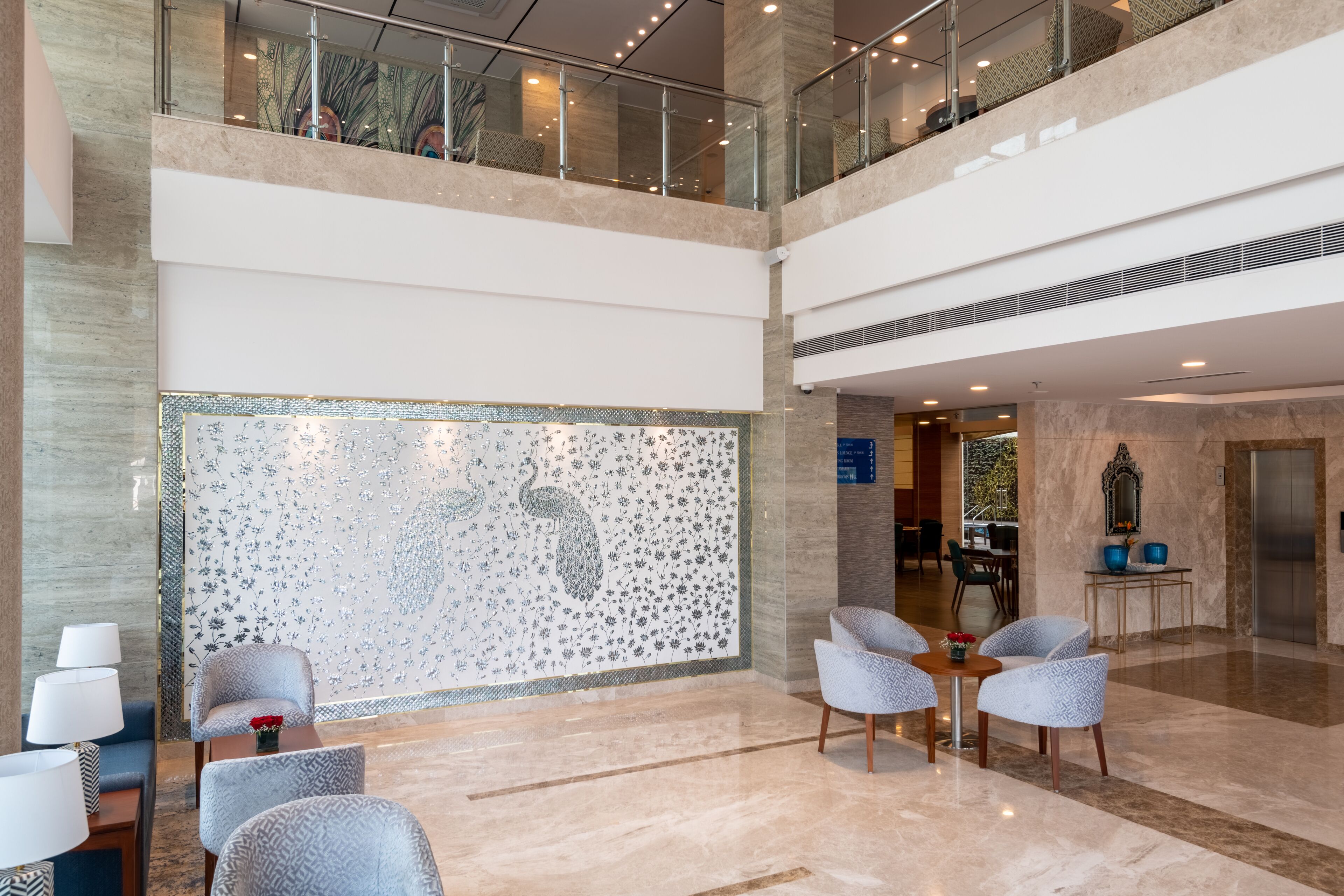 A spacious lobby with a high ceiling, a decorative wall with a peacock design, and a seating area with patterned chairs.