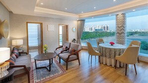 A modern living room with a sofa, chairs, a table, and a view of a cityscape. - ExpoInn Suites and Convention (Greater Noida)