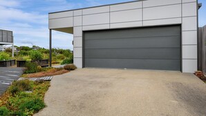 A modern building with a large garage door, surrounded by a landscaped garden and a wooden deck. - Whales & Wombats (Bass Coast)