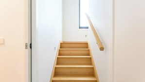A wooden staircase in a room with white walls and a small window at the top. - Whales & Wombats (Bass Coast)