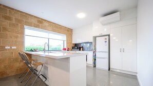 A modern kitchen with white cabinets, a large window, and a built-in island with bar stools. - Whales & Wombats (Bass Coast)