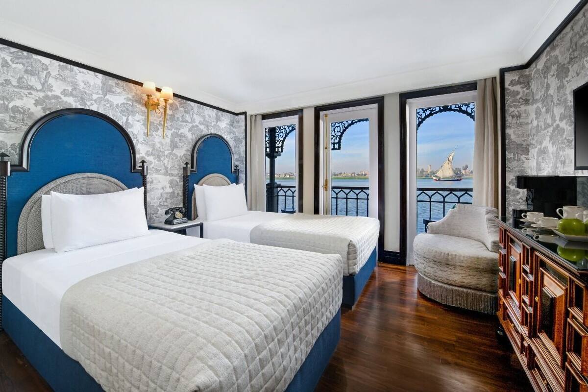 A hotel room with two beds, a sitting area, and a view of a river and bridge.