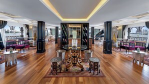 A luxurious interior with a grand piano, ornate furniture, and a view of a river. - Movenpick SS Misr. Monday - Friday (Luxor)