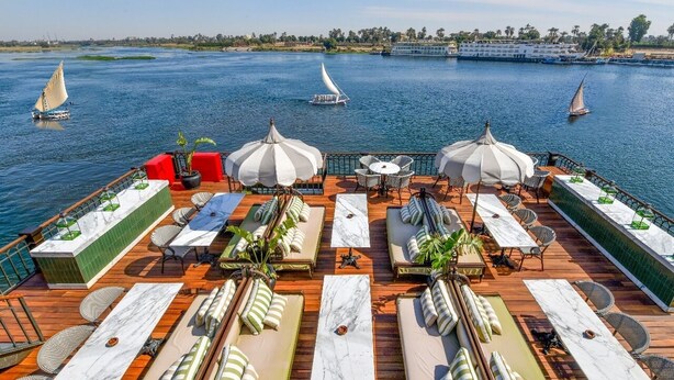 A deck with outdoor seating, a pool, and a view of the water. - Movenpick SS Misr. Monday - Friday (Luxor)