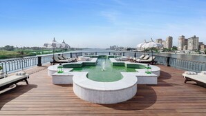 A rooftop pool area with lounge chairs and a central water feature, overlooking a river and cityscape. - Movenpick SS Misr. Monday - Friday (Luxor)