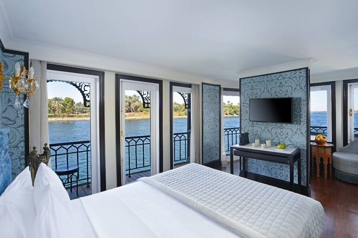 A spacious bedroom with a large bed, a TV mounted on the wall, and a balcony with a view of the water.