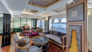 A luxurious room with a large window overlooking a body of water, ornate ceiling design, and classic furniture. - Movenpick SS Misr. Monday - Friday (Luxor)