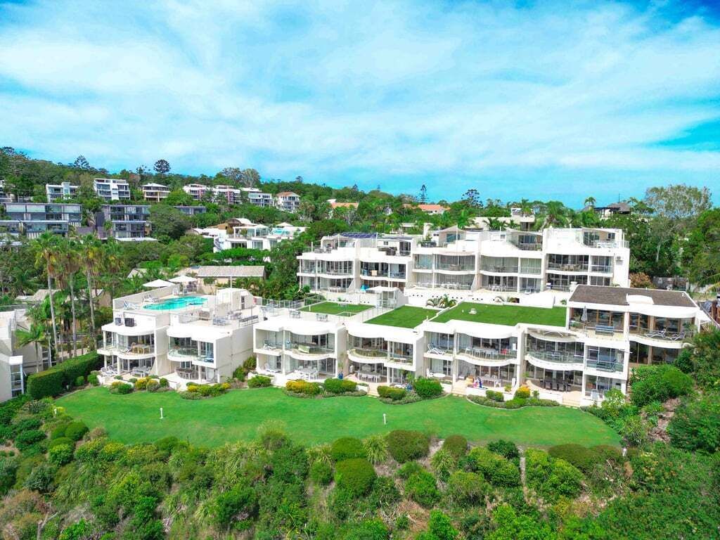 A modern multi-story hotel with a pool, surrounded by lush greenery and other buildings.