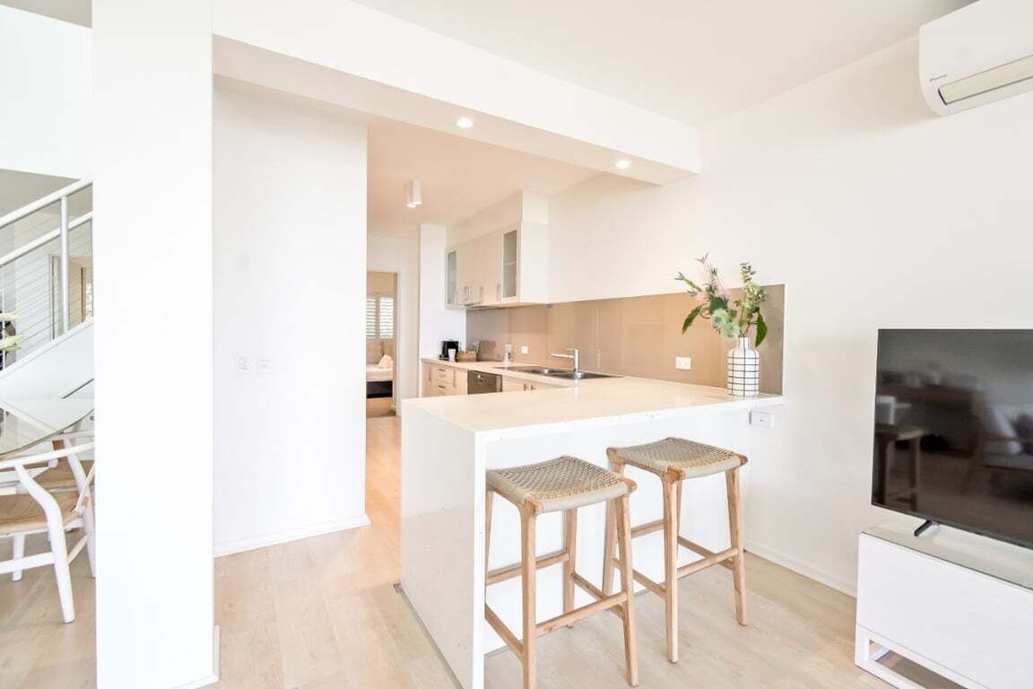 A modern kitchen with a central island, bar stools, a TV, and a staircase.