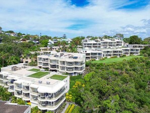 Un hôtel à plusieurs étages doté de balcons, d’un jardin sur le toit et d’une végétation luxuriante qui entoure l’établissement.