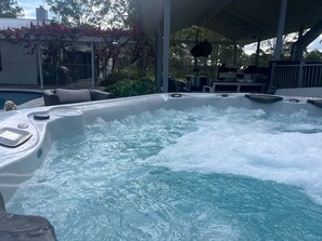 Un jacuzzi con panel de control, rodeado de mobiliario exterior y una zona de terraza cubierta.