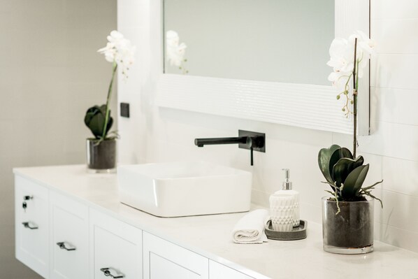 A bathroom with a white sink, a mirror, and two potted plants.