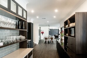 A modern kitchen with dark cabinetry, a dining area with a table and chairs, and a hallway leading to a living space.
