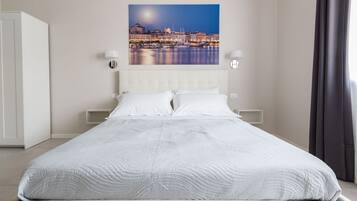 Una cama bien hecha con colcha blanca, cabecera y dos lámparas de noche.
