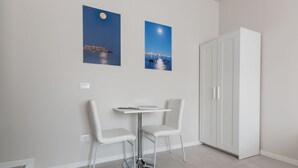 A modern room with a white table and two chairs, a wardrobe, and two framed pictures of a night scene with a moon and a boat. - PhotoRooms B&B (Syracuse)