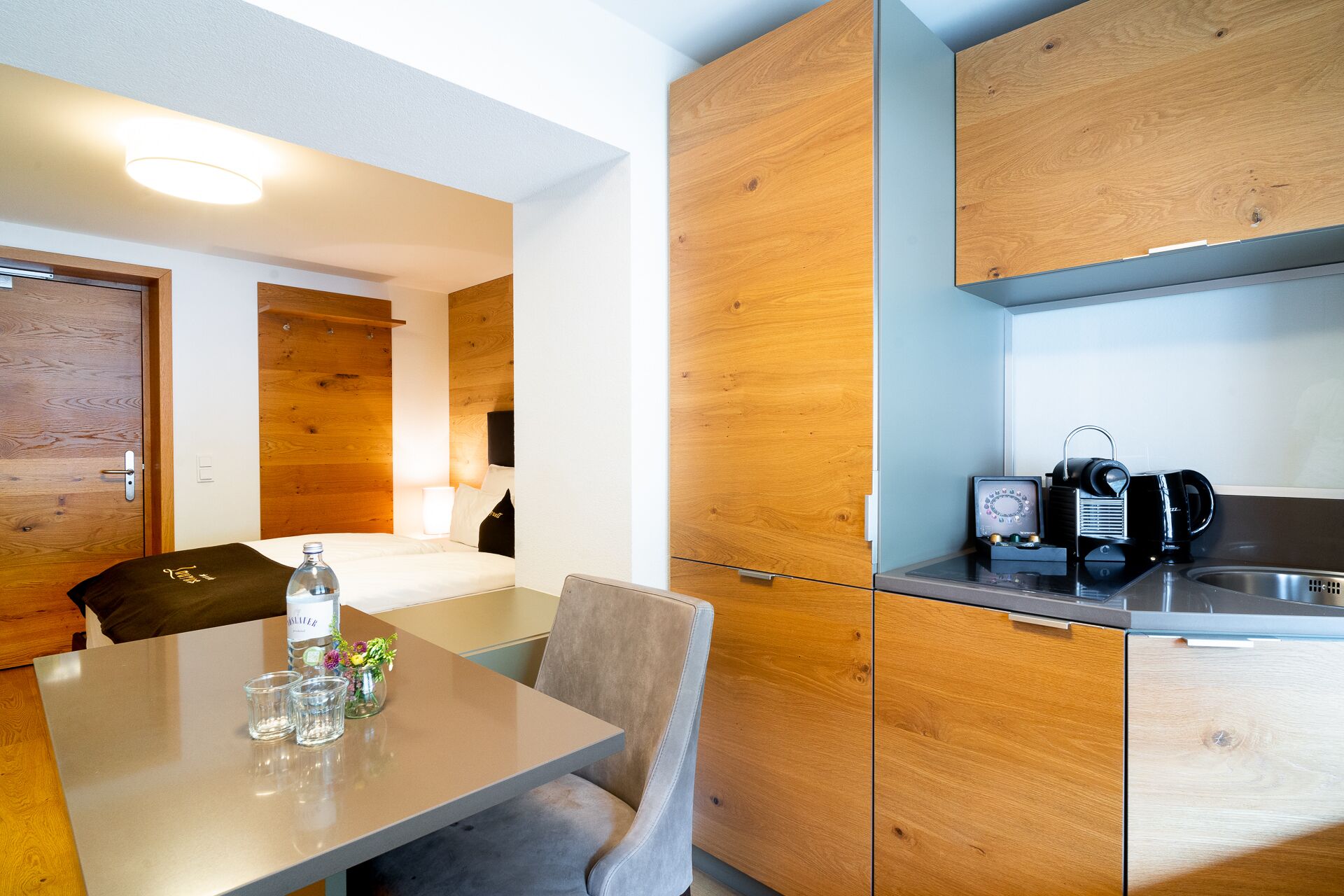 A compact hotel room with a kitchenette, a dining area, and a bed.