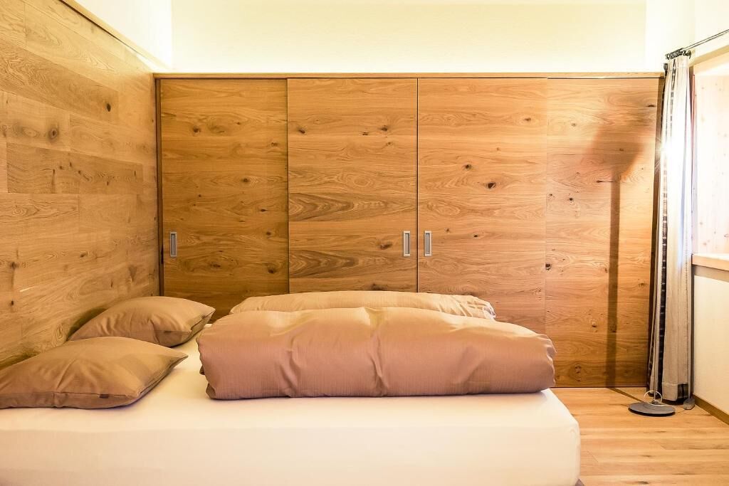 A bedroom with a wooden wardrobe, a bed with beige bedding, and a bedside table.