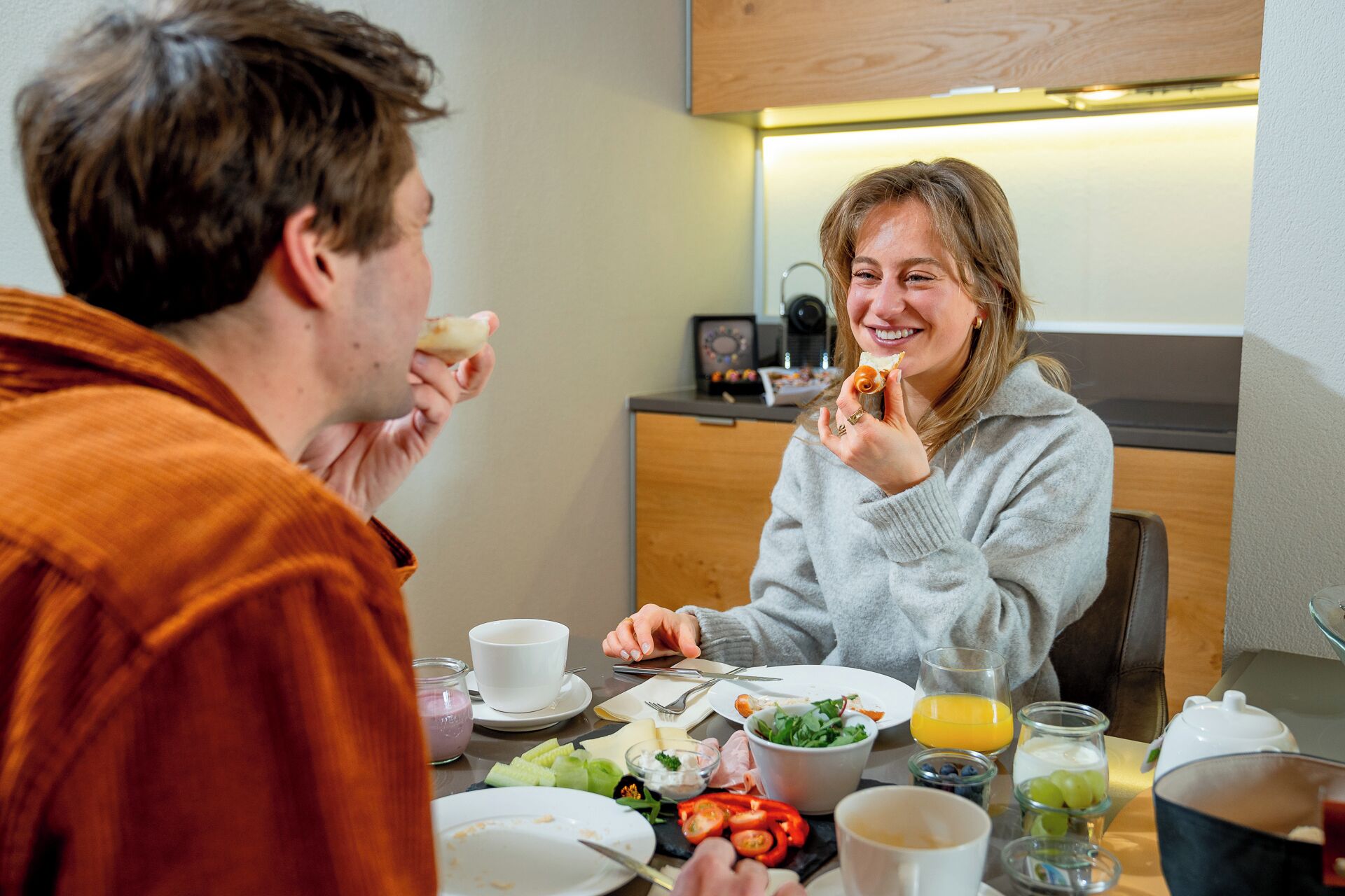 Een ontbijtsetting met een gedekte tafel voor twee personen, inclusief borden, bestek, een saladeschaal en een glas sinaasappelsap.