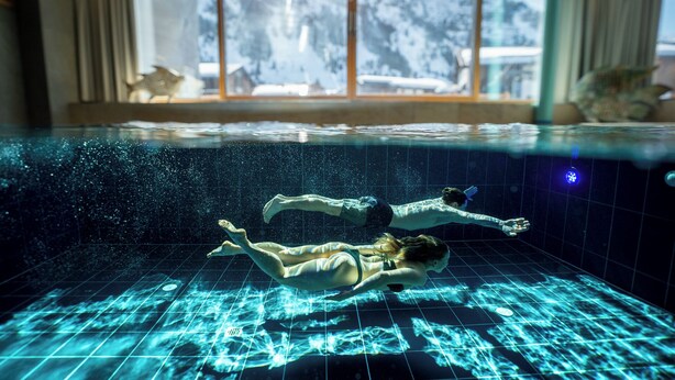 An indoor swimming pool with a view of snowy mountains through a window. - Apart-Hotel Laurus (Lech am Arlberg)