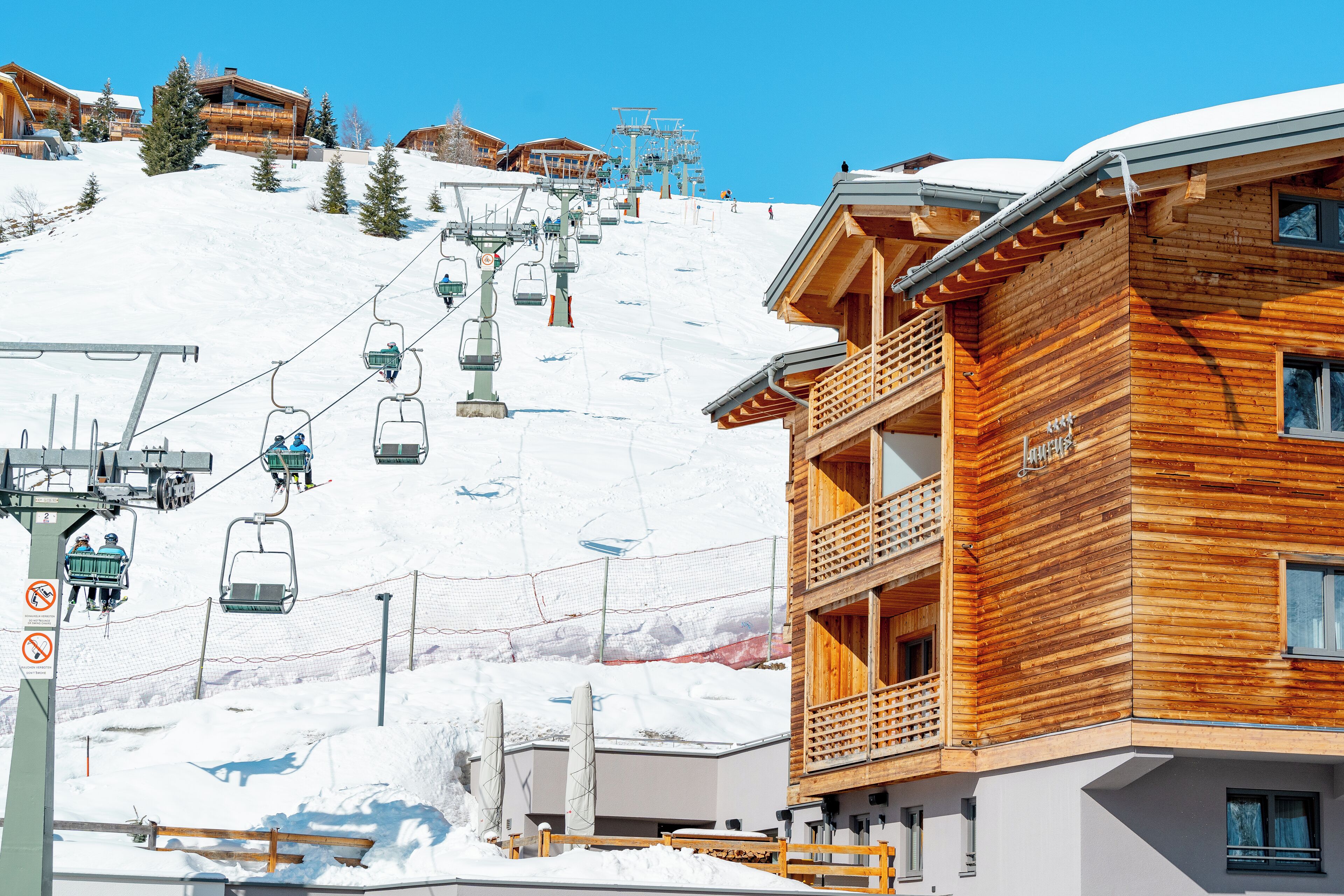 Un bâtiment en bois doté de balcons, un télésiège et une pente enneigée.
