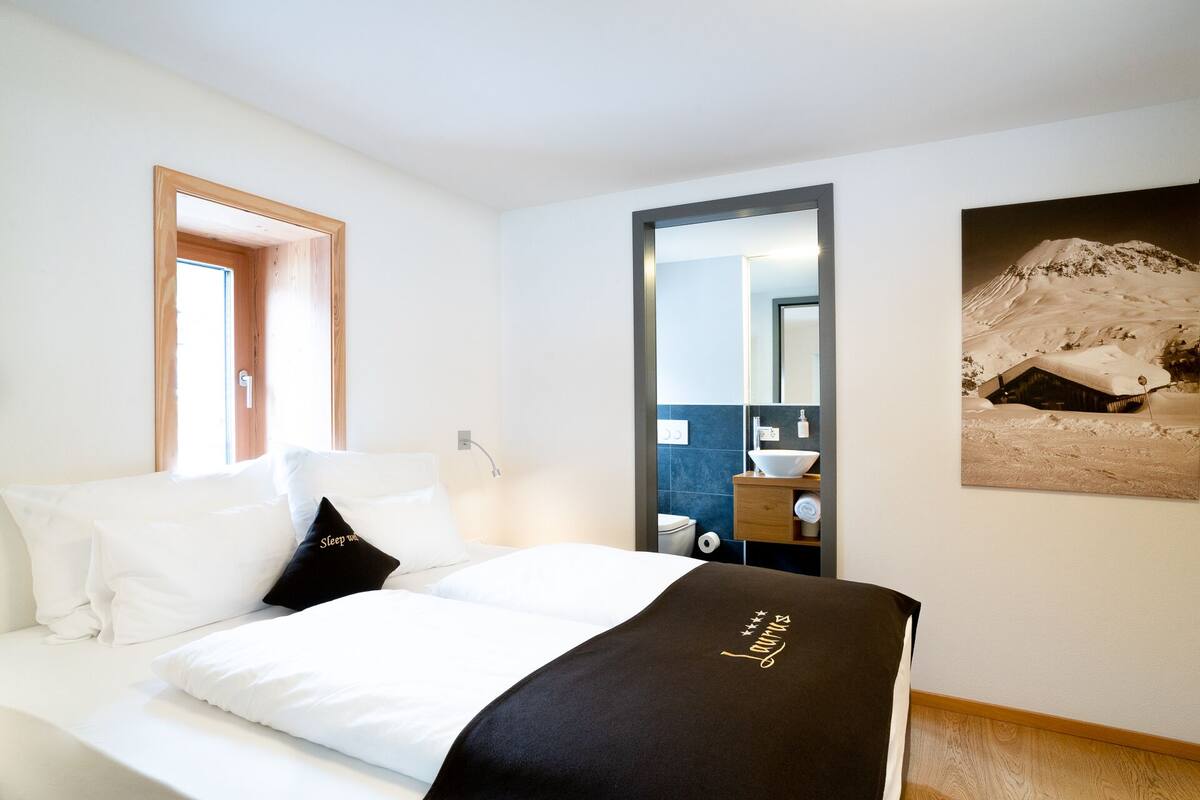 A hotel room with a bed, a bathroom visible through an open door, and a framed picture on the wall.