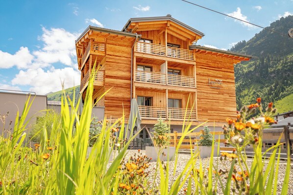 A wooden multi-story building with balconies, surrounded by greenery and a mountainous backdrop. - Apart-Hotel Laurus (Lech am Arlberg)