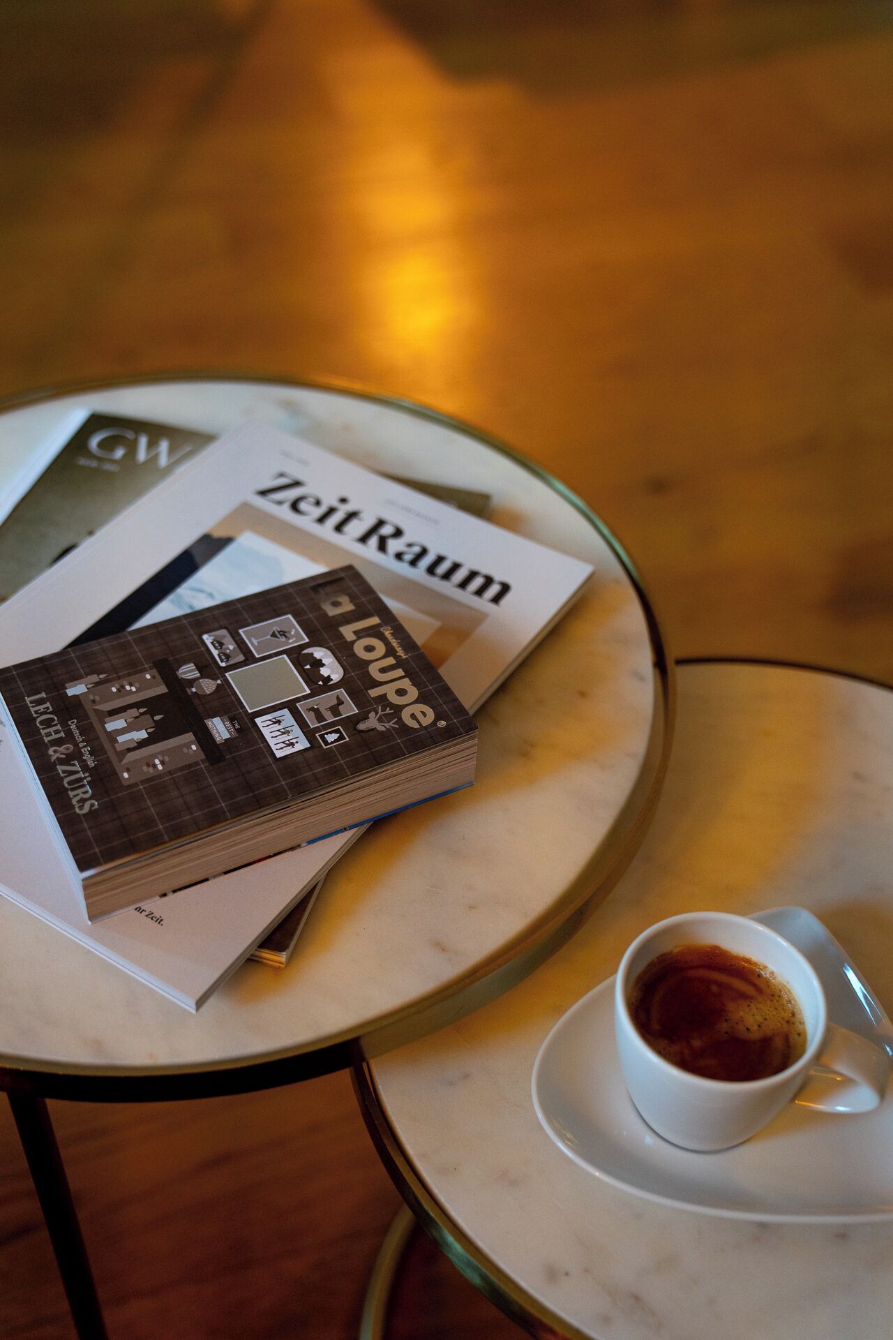 A table with a stack of books titled 'ZeitRaum' and a cup of coffee on a saucer.