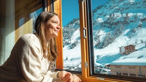 A person sitting by a window with a view of a snowy mountain landscape. - Apart-Hotel Laurus (Lech am Arlberg)