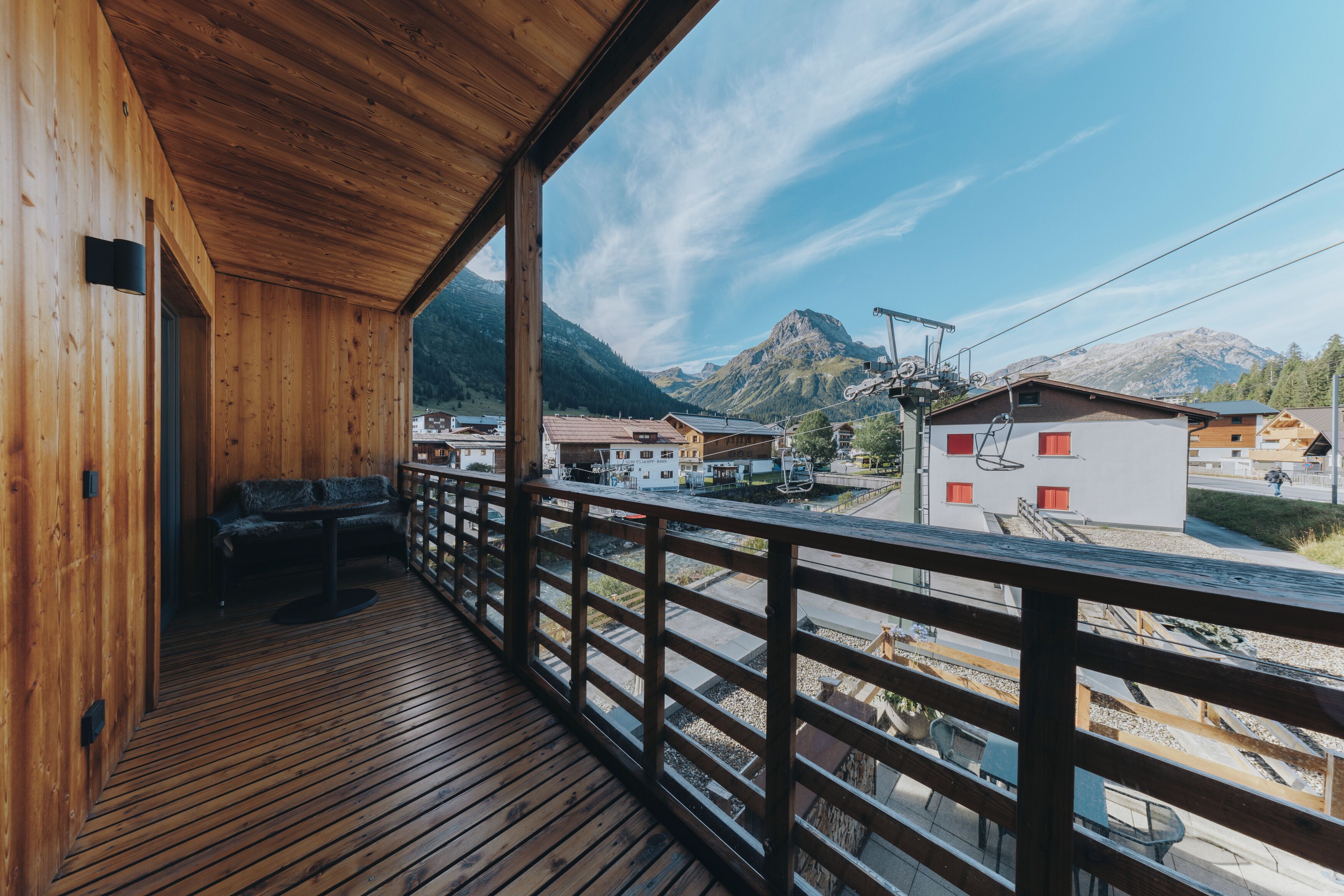 Un balcón de madera con vistas a una cadena montañosa y un pueblo pequeño en la falda.